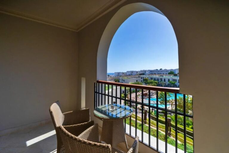 A balcony under an arch, with two woven armchairs, above the pools and the gardens