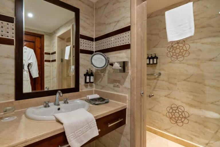 A bright bathroom with a sink, a dark-framed mirror and a glass shower