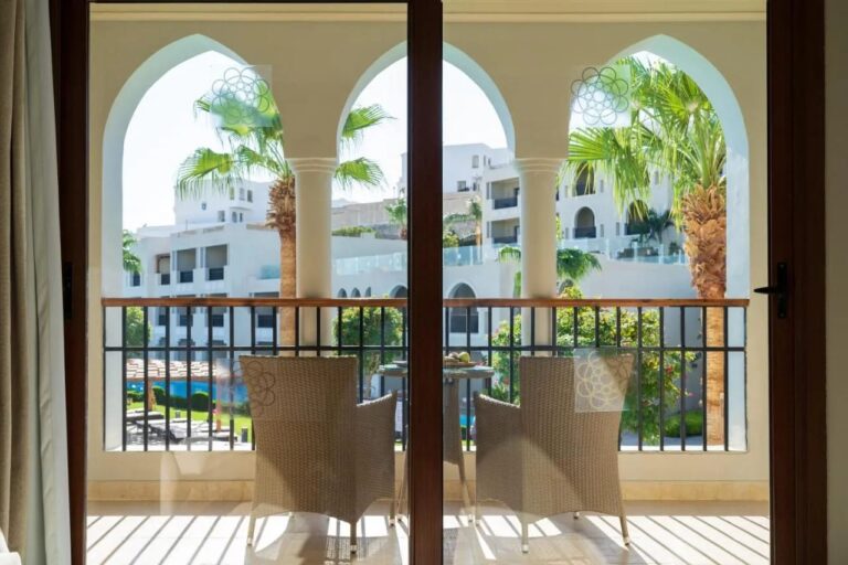 An arcaded balcony with two woven armchairs, facing the palm trees and the white buildings of Sunrise Arabian Beach Resort