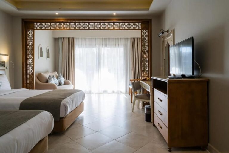 A twin room with a chest of drawers, a TV and a seating area in front of the picture window