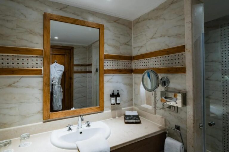 A bathroom with a sink, a light wood-framed mirror and a mosaic frieze
