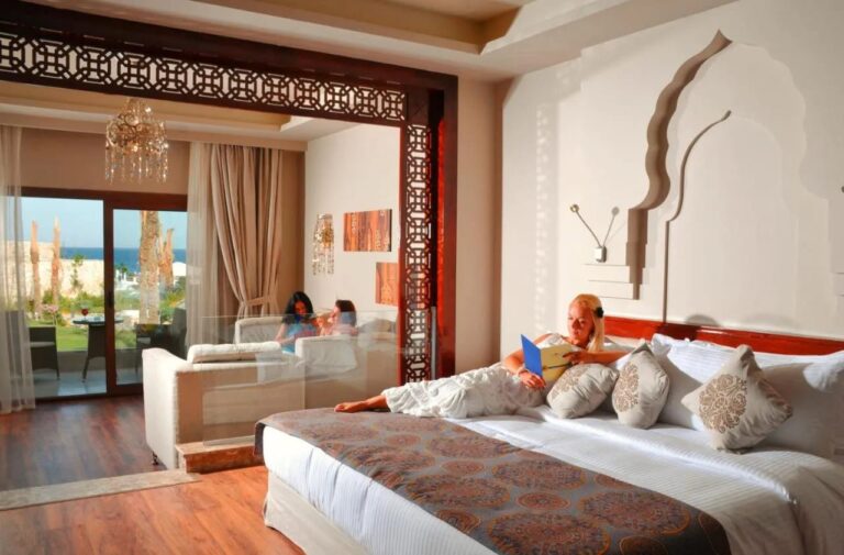 A room with a wooden floor, a double bed, a seating area under a chandelier and a sea-facing terrace