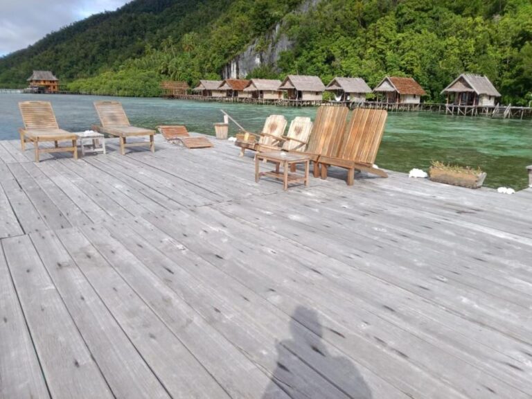 A wooden jetty with sun loungers, facing the row of bungalows on stilts