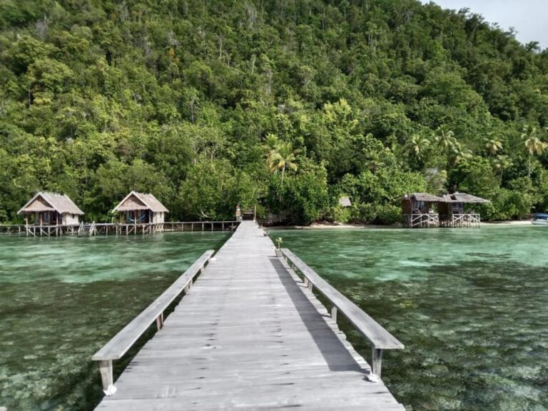A long jetty with benches leading to the shore, between the bungalows of Terimakasih Homestay