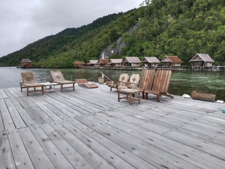 Sun loungers on a jetty on a gray day, in front of the bungalows and the hill