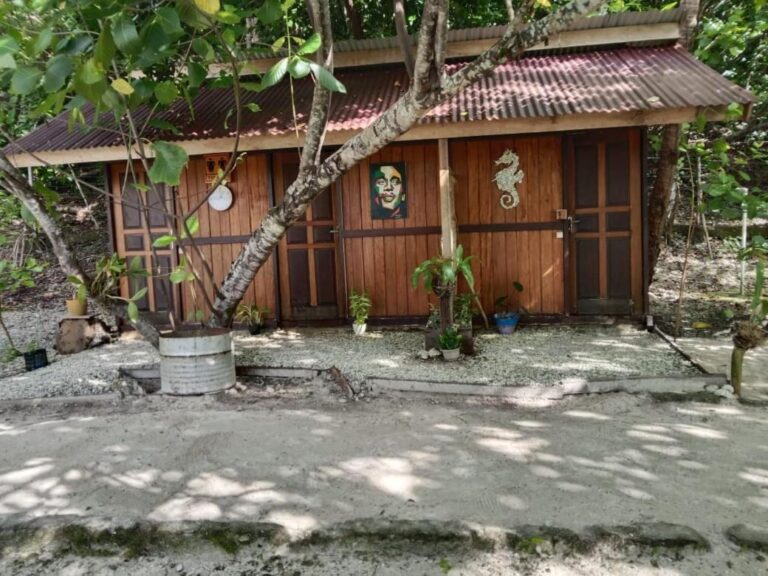 The toilet hut, in wood and red tin, in the sun beside a sandy path