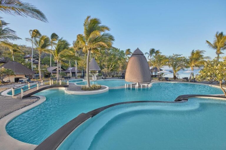 The curved pool, with a wooden footbridge and a thatched kiosk, under the palm trees
