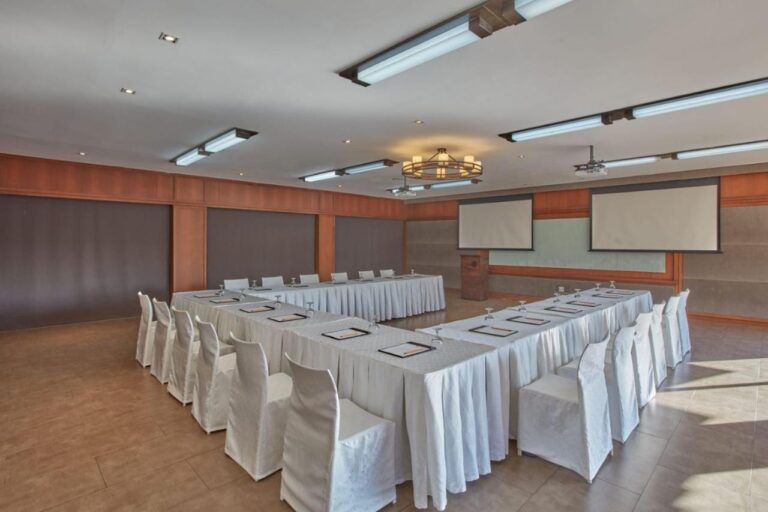 A meeting room with U-shaped tables in white tablecloths and two projection screens