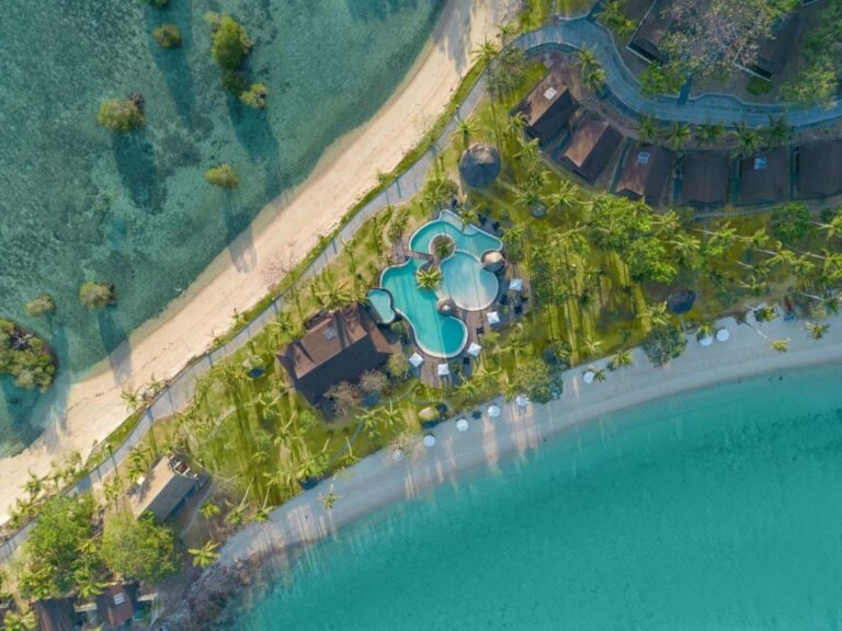 Aerial view of the pool and the resort roofs, between two sandy beaches