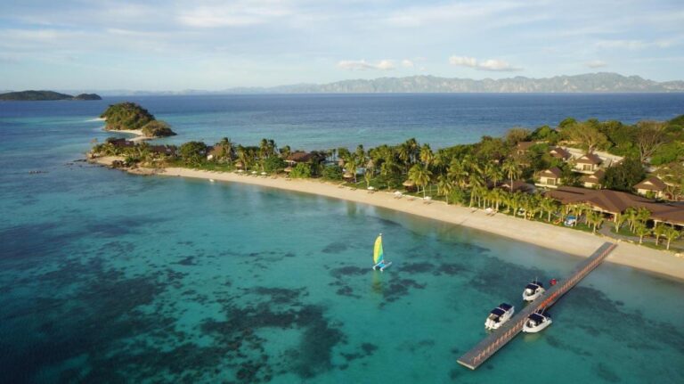 Aerial view of the beach, the jetty with three boats and a small sailing catamaran
