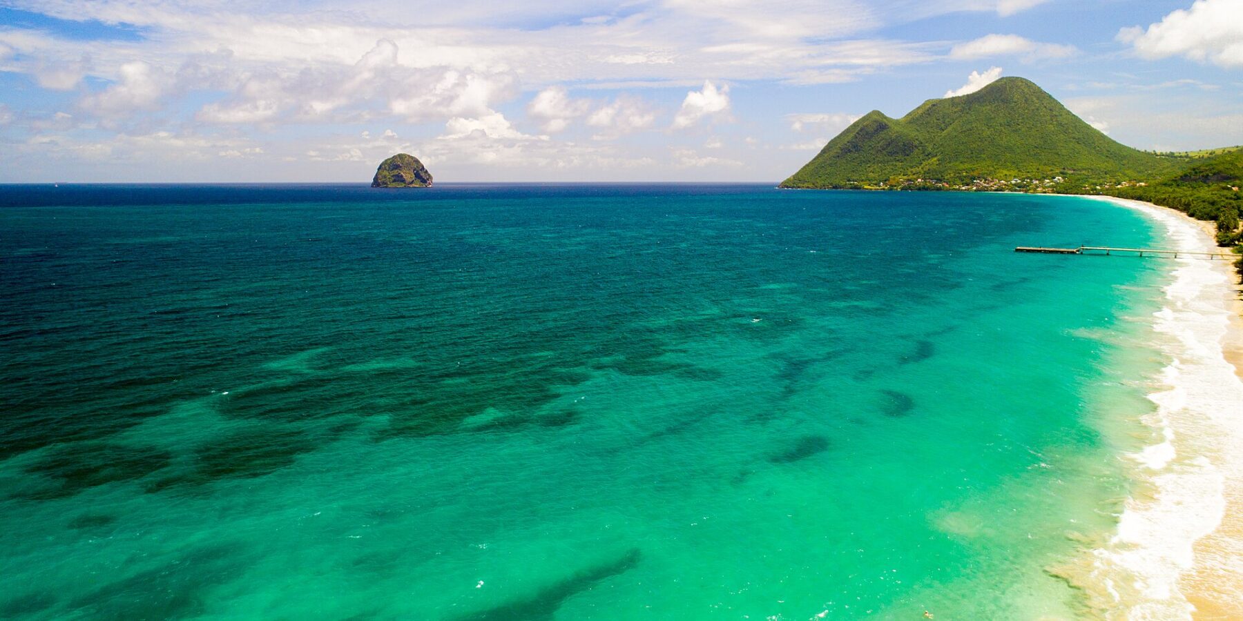 Aerial view of the long Le Diamant beach lined with turquoise water, Diamond Rock offshore and Morne Larcher, a green hill, on the right