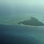 Misali Island seen from a plane, a triangle of forest edged by a white beach, sitting on a turquoise reef flat in a dark blue sea, in the haze