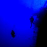 In deep blue water, two divers in silhouette follow the stern railing of the Salem Express, the tilted deck on the right