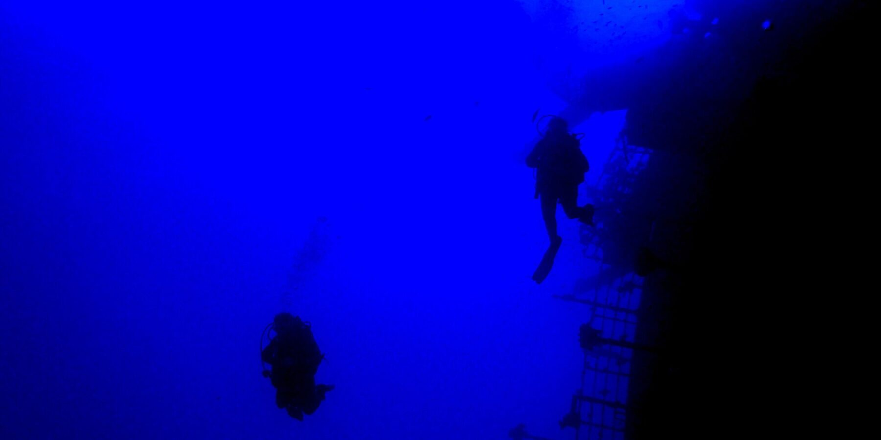 In deep blue water, two divers in silhouette follow the stern railing of the Salem Express, the tilted deck on the right