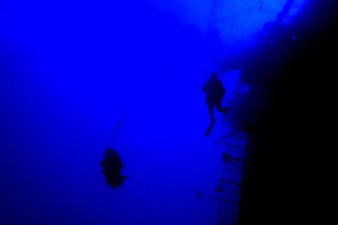 In deep blue water, two divers in silhouette follow the stern railing of the Salem Express, the tilted deck on the right